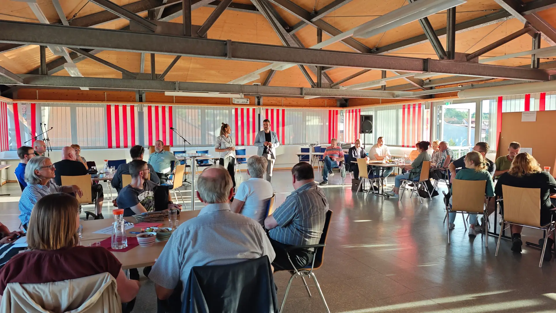 Teilnehmende eines Ideenworkshops sitzen an Tischen in einem Raum.